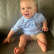 Darren is registered to the contest to win money with this photo: baby, child, polo_shirt, shorts, sitting, couch, leather, foot, hand, face, happy, smiling, blue, striped, skin, indoors, person, young_child, expression, casual_clothing
