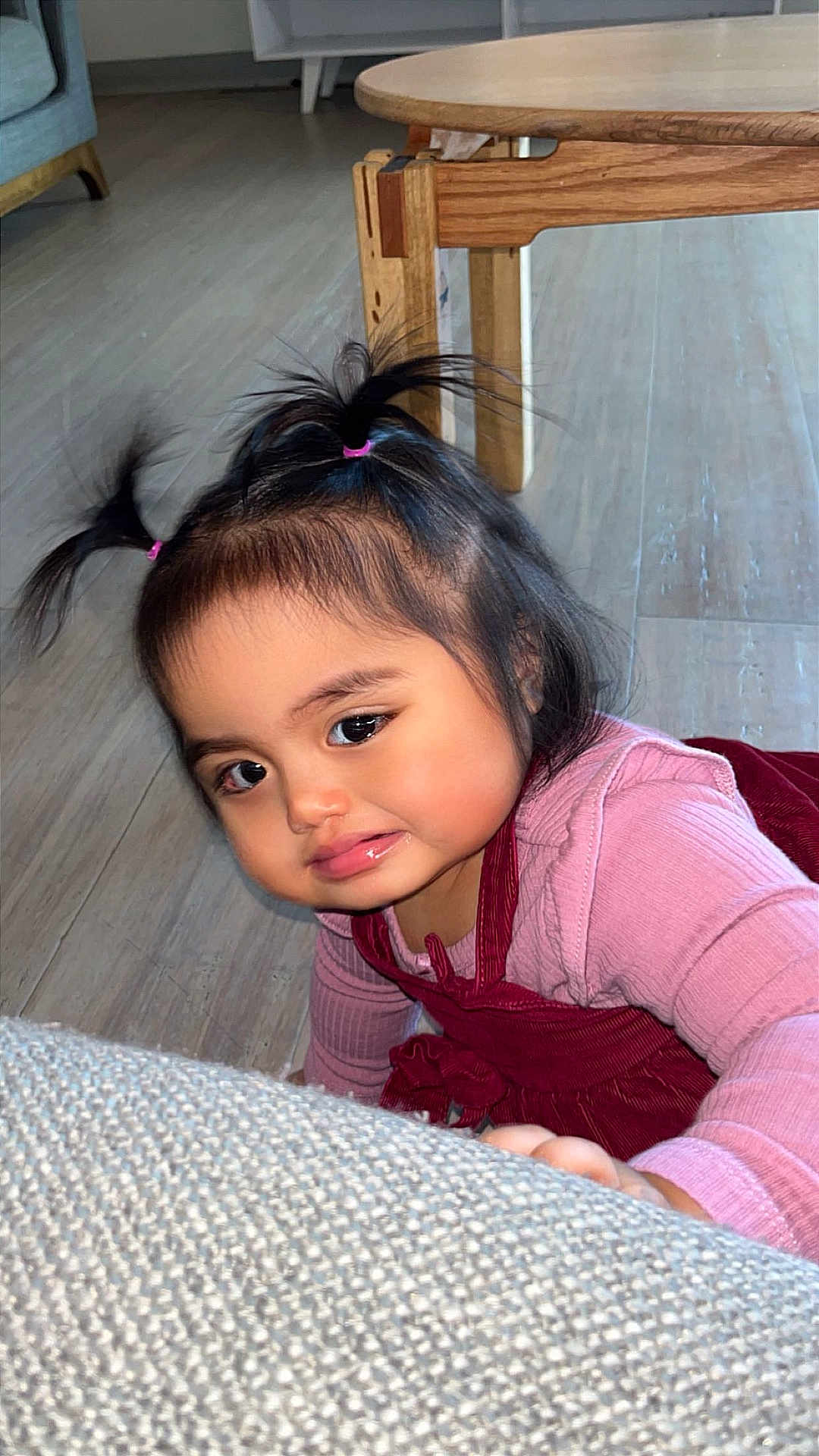 Emillia is registered to the contest to win money with this photo: child, toddler, baby, indoor, hardwood_floor, wooden_table, sofa, pink_clothing, red_dress, hair_ties, pigtails, cute, crawling, floor, big_eyes, chubby_cheeks, close_up, living_room, furniture, sofa_texture
