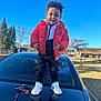 Shai is registered to the contest to win money with this photo: black_car, blue_sky, car, casual_clothing, child, curly_hair, daylight, happy, keychain, outdoor, pavement, person, red_jacket, smile, sneakers, standing, suburb, sunny, toddler, trees