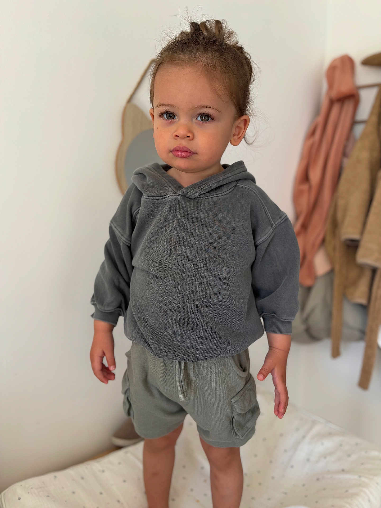 Adel a rejoint le concours — aidez-le/la à gagner de superbes lots ! toddler, child, hoodie, shorts, standing, bed, indoor, mirror, coat, clothing, face, hair, expression, curious, casual, portrait, young_child, home, soft_light, furniture