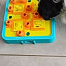 dog, black_and_white, toy, puzzle, interactive_toy, floor, tile_floor, pet, animal, sniffing, play, curious, indoor, plastic_toy, orange, yellow, blue, small_dog, close_up, head