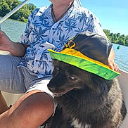 Poka participe au concours pour gagner de l'argent avec cette photo : man, dog, hat, boat, lake, water, trees, summer, sunlight, sunglasses, tropical_shirt, black_dog, outdoor, nature, pet, canine, leisure, vacation, people, animal