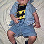 baby, batman, blanket, casual, child, clothing, cute, denim_shirt, denim_shorts, face, fashion, footwear, indoors, infant, lying_down, person, portrait, sneakers, tshirt, young