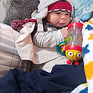 Arlo joined the competition — help win amazing prizes! baby, child, hat, knit_hat, toy, colorful_toy, blanket, pillow, indoor, cute, cozy, infant, clothing, striped_shirt, smiling, face, hand, warm, soft, play