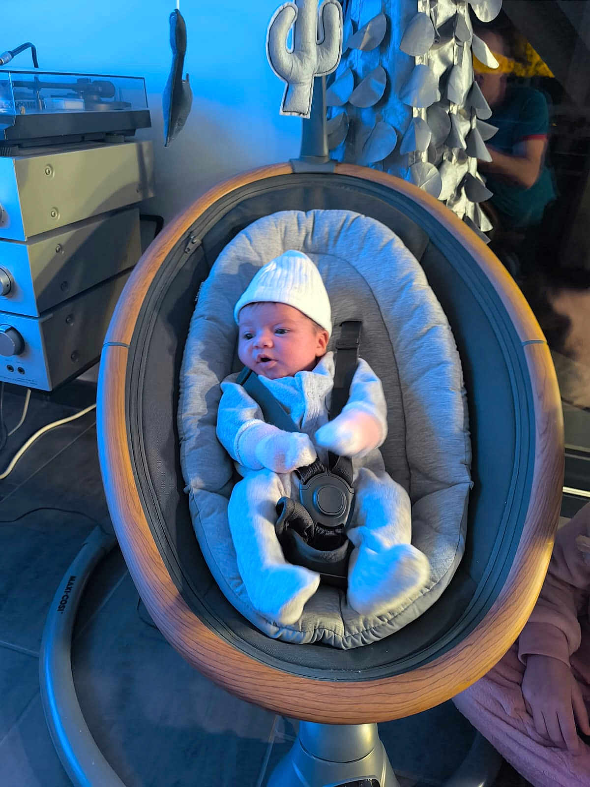 Camélia participe au concours pour gagner de l'argent avec cette photo : baby, infant, baby_rocker, wooden_frame, white_hat, soft_clothing, baby_bonding, indoor, modern_design, turntable, decorative_wall, curious_baby, child, seat_belt, cushion, person, floor, home_interior, light_blue, relaxing