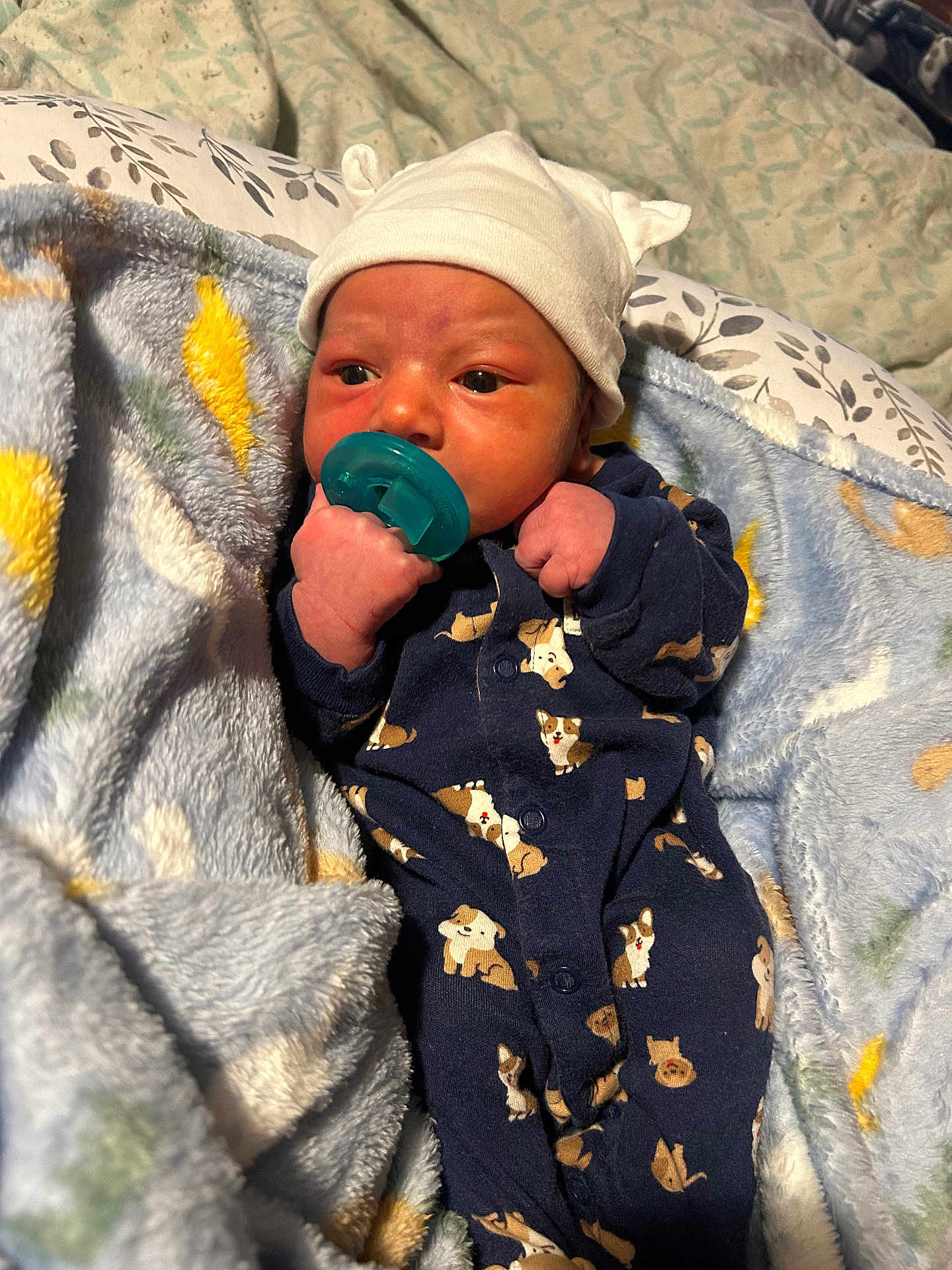Amari is registered to the contest to win money with this photo: newborn, baby, pacifier, onesie, hat, blanket, infant, cute, sleepwear, cozy, soft, patterned_clothing, clothing, face, person, hand, bed, resting, indoor, child