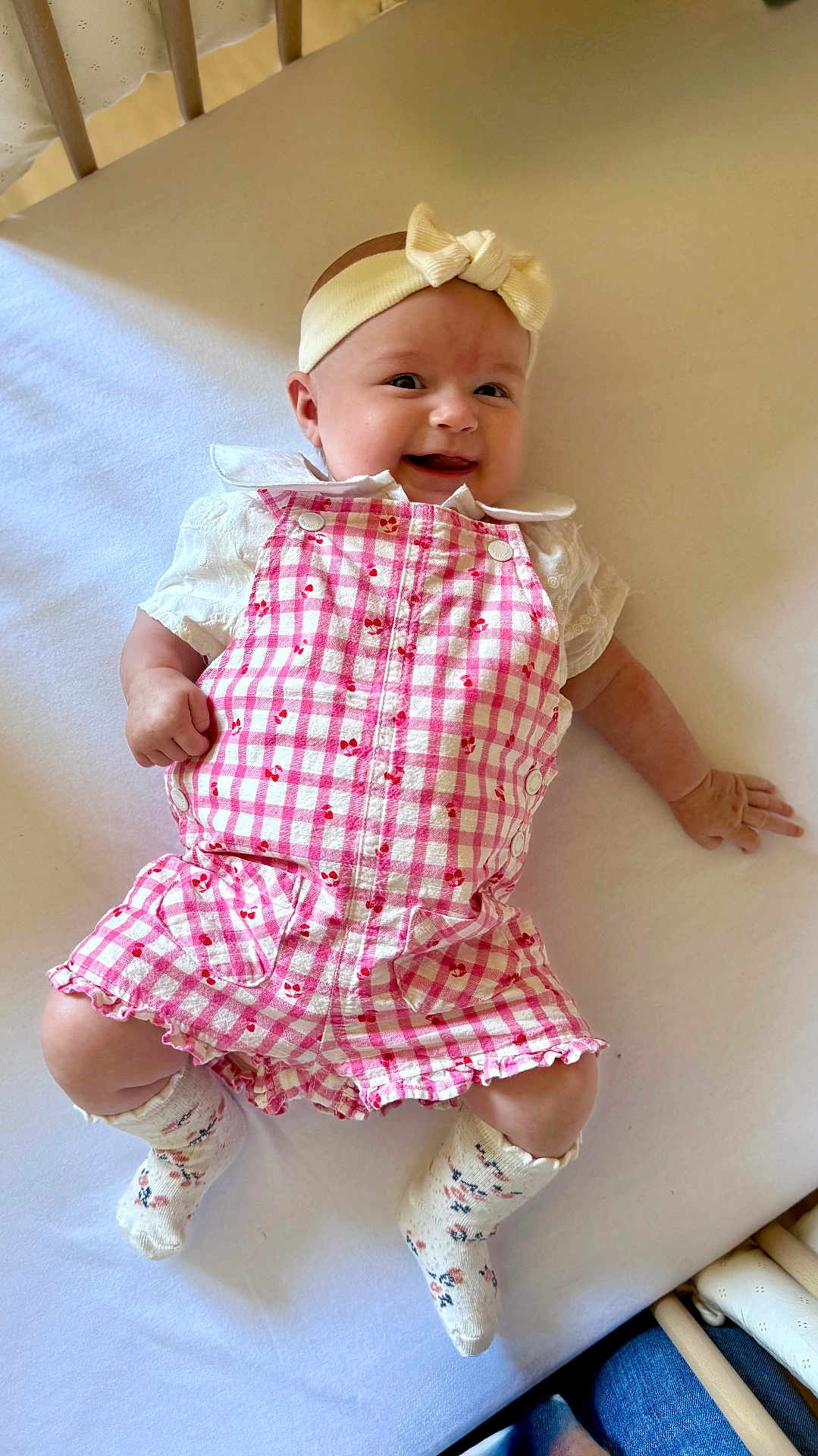 Constance participe au concours pour gagner de l'argent avec cette photo : baby, infant, smiling, headband, pink_clothing, romper, crib, white_sheet, socks, cute, happy, child, person, lying_down, indoors, baby_clothes, headwear, soft_lighting, cheerful, small_hands
