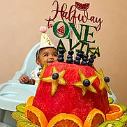 Avika joined the competition — help win amazing prizes! baby, child, half_birthday, party_hat, high_chair, watermelon, fruit_cake, blueberries, starfruit, orange_slices, kiwi, celebration, smiling, food, plate, indoor, person, happy, birthday, decorations