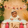 Avika is registered to the contest to win money with this photo: baby, child, party_hat, high_chair, tassels, milestone, birthday, half_year, decorations, flowers, banner, photos, smiling, celebration, indoor, cute, person, headwear, infant, happy
