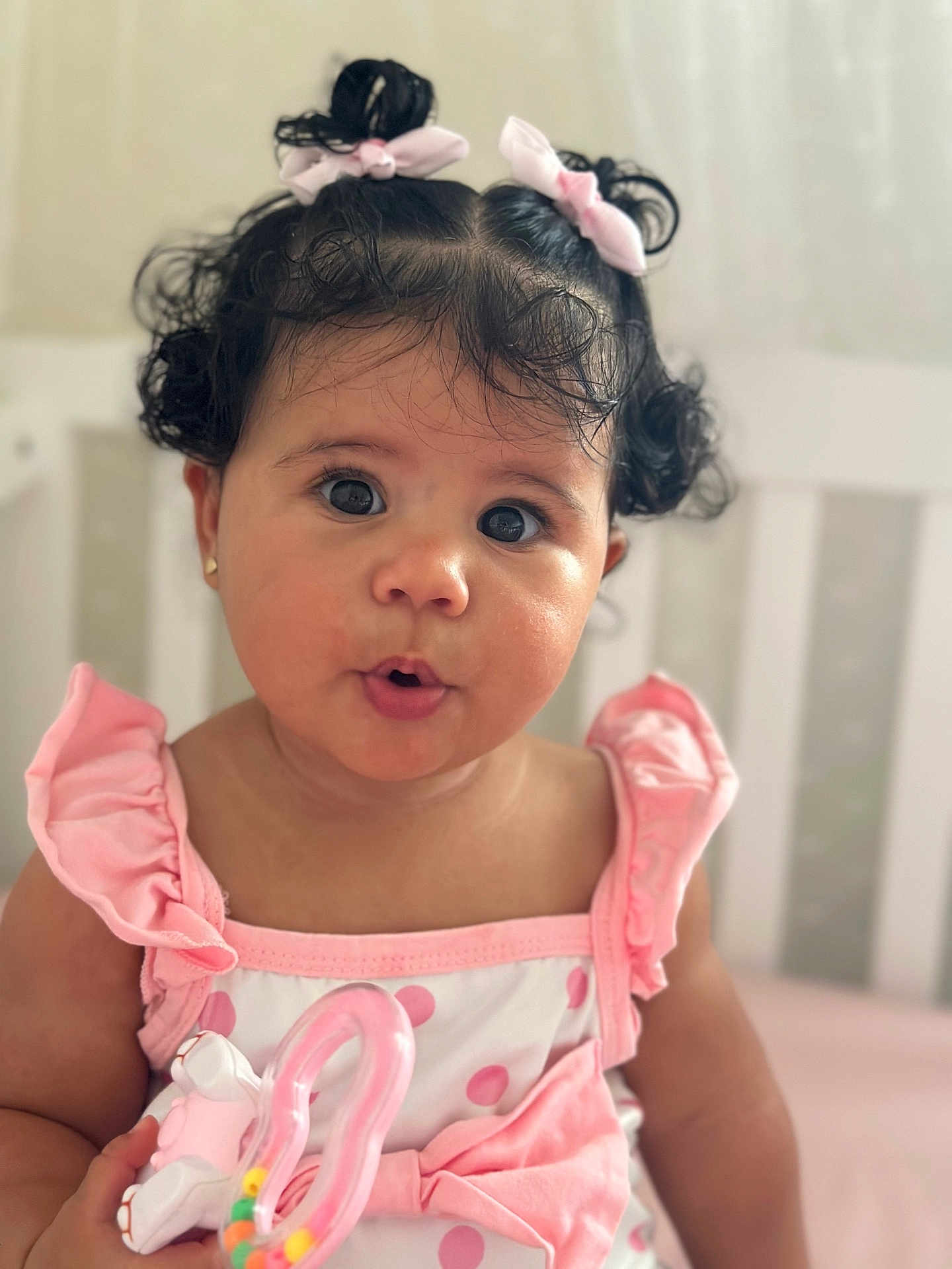 Joanna joined the competition — help win amazing prizes! baby, child, girl, curly_hair, pigtails, pink_bows, pink_dress, polka_dots, toy, nursery, crib, cute_expression, indoors, portrait, soft_lighting, infant, sitting, closeup, adorable, person