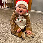 Brady is registered to the contest to win money with this photo: baby, child, smiling, holiday, christmas_hat, reindeer_onesie, carpet, indoors, festive, cute, happy, person, floor, decoration, toy, warm_clothing, knit_hat, seasonal, holiday_decor, baby_clothes