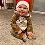 baby, child, smiling, holiday, christmas_hat, reindeer_onesie, carpet, indoors, festive, cute, happy, person, floor, decoration, toy, warm_clothing, knit_hat, seasonal, holiday_decor, baby_clothes