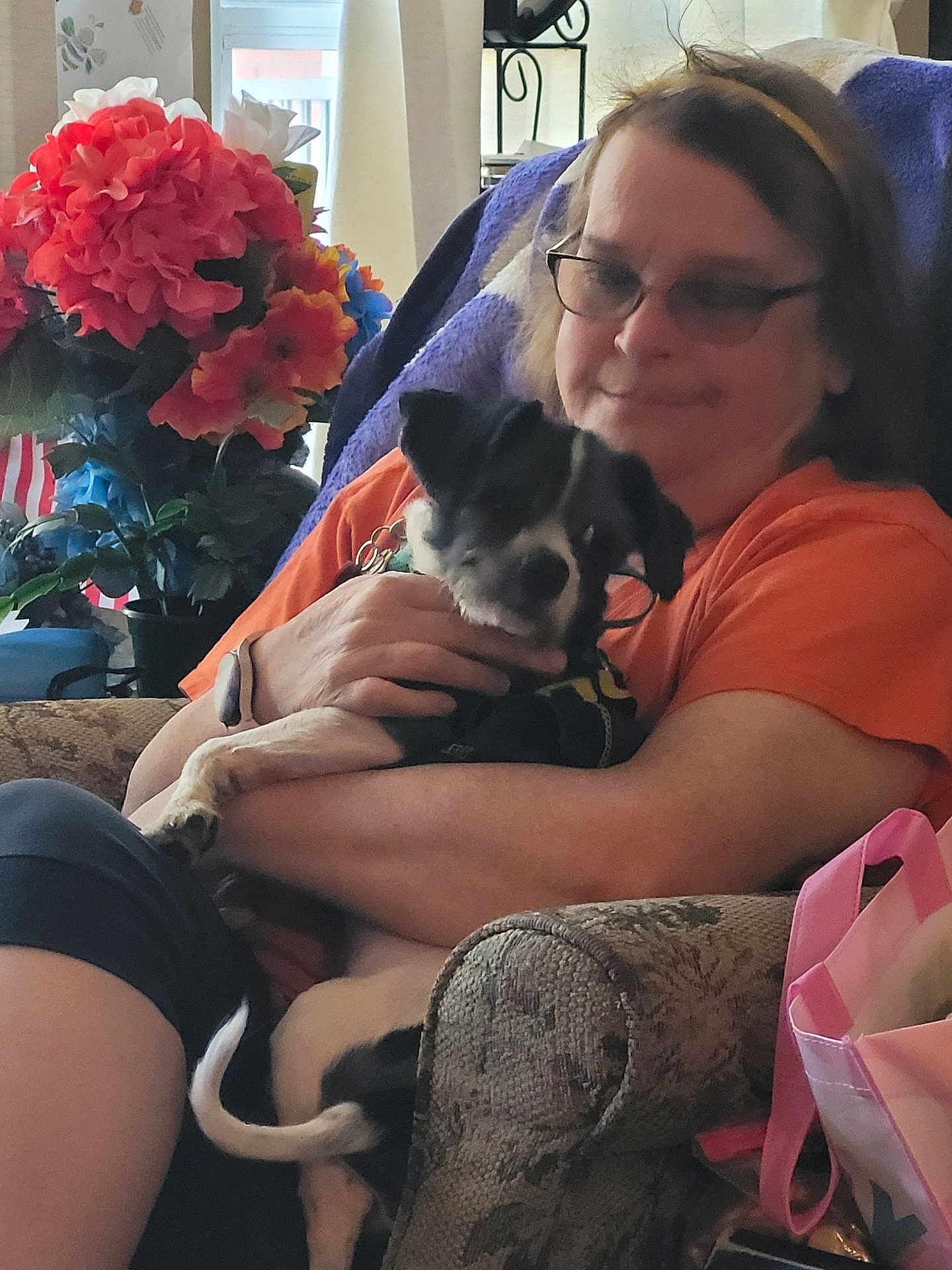 Brody joined the competition — help win amazing prizes! person, dog, indoor, armchair, flowers, glasses, orange_shirt, pet, comfort, seated, tote_bag, black_and_white_dog, hand, home, decor, relaxation, casual, fur, tail, love