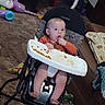 baby, child, infant, walker, highchair, snack, eating, hand, face, portrait, sitting, indoor, living_room, carpet, couch, toys, playroom, orange_shirt, barefoot, cosco