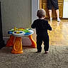 Koda is registered to the contest to win money with this photo: toddler, child, baby, walking, back_view, indoor, home, kitchen, carpet, floor, activity_table, toy, playtime, adult, supervision, family, furniture, wooden_floor, casual_clothing, candid_photo