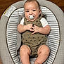 baby, pacifier, infant, baby_seat, cushion, clothing, dinosaur_pattern, wooden_floor, cute, chubby, smiling, hands, legs, feet, portrait, indoor, comfortable, relaxed, child, person