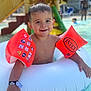 child, toddler, pool, water, floaties, inflatable_ring, swimming, summer, wet_hair, smiling, outdoor, playground, slide, water_play, fun, happy, vacation, sunlight, recreation, leisure