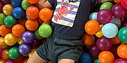 Jules a rejoint le concours — aidez-le/la à gagner de superbes lots ! child, toddler, ball_pit, colorful, plastic_balls, joyful, smiling, clothing, shorts, playing, happy, indoor, fun, leisure, cute, face, person, casual_wear, entertainment, expression