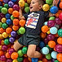 child, toddler, ball_pit, colorful, plastic_balls, joyful, smiling, clothing, shorts, playing, happy, indoor, fun, leisure, cute, face, person, casual_wear, entertainment, expression