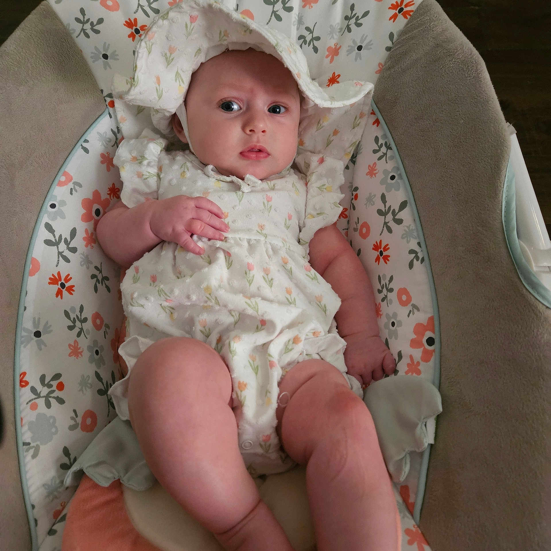 Jocelynn joined the competition — help win amazing prizes! baby, baby_seat, bonnet, child, comfortable, curious_expression, cute, floral_outfit, flower_print, green, indoor, infant, orange, patterned_cushion, pink, portrait, small_feet, small_hands, soft_lighting, white