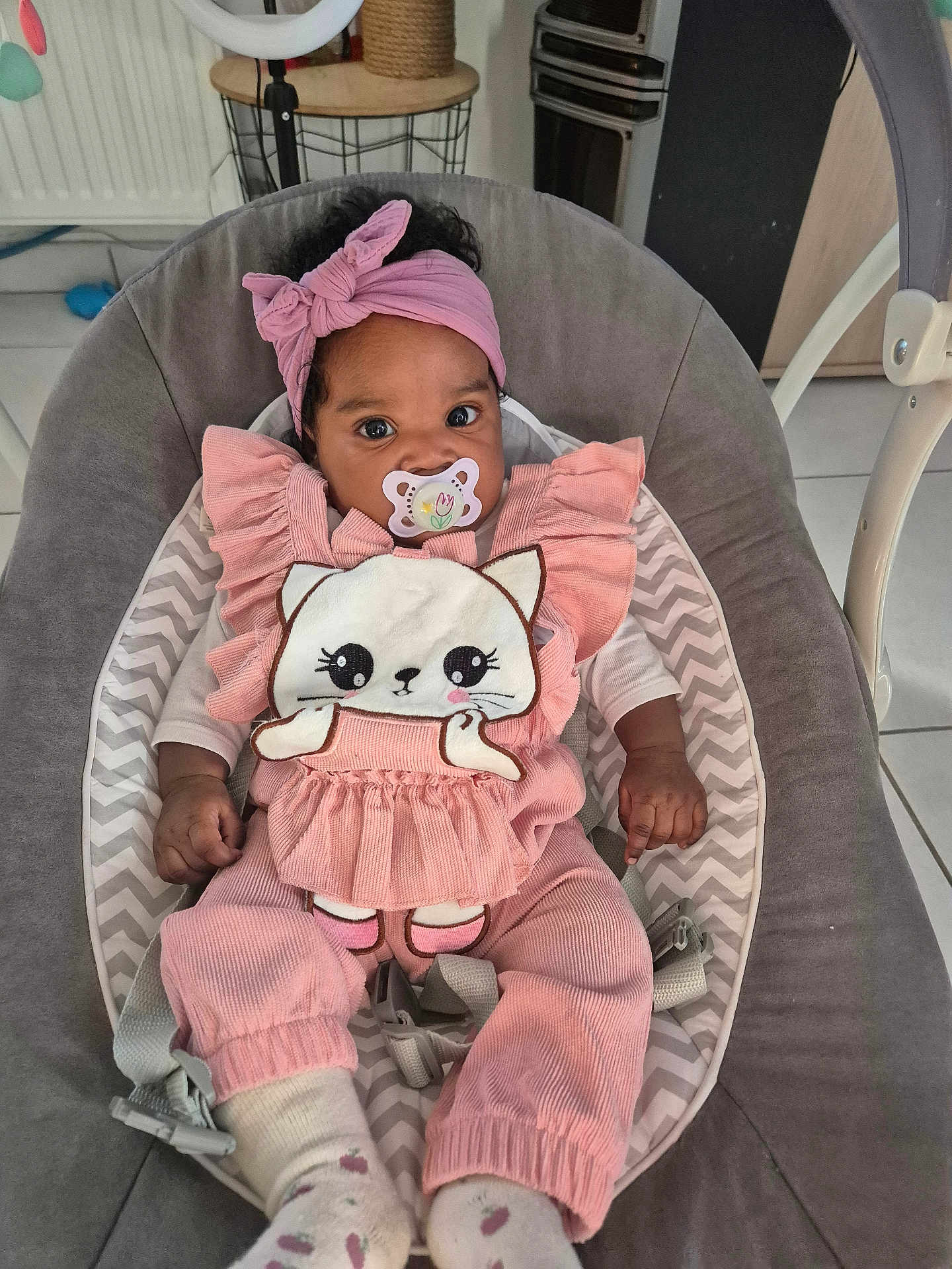 Haïly a rejoint le concours — aidez-le/la à gagner de superbes lots ! baby, infant, pacifier, pink_clothing, headband, baby_seat, cute, indoors, child, toddler, soft_toys, patterned_socks, relaxed, adorable, person, smiling_eyes, furniture, home, comfort, portrait