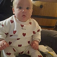 Khloé participe au concours pour gagner de l'argent avec cette photo : baby, casual_wear, child, curious_expression, cute, face, floor_mat, footwear, hands, heart_pattern, indoor, infant, person, plush_toy, sitting, soft_lighting, toddler, white_clothing, wooden_background, young_child