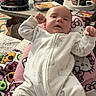 baby, infant, onesie, animal_print, person, pink_pajamas, hello_kitty, living_room, furniture, blanket, clothing, footwear, smile, relaxing, indoor, home, table, bottle, couch, cozy
