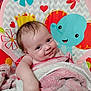 baby, smiling, blanket, playmat, elephant, flower, heart, child, infant, cute, pink, white, cozy, happy, lying_down, indoors, young_child, soft_texture, colorful, portrait
