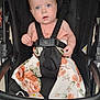 baby, child, stroller, safety_harness, blue_eyes, curious, drool, floral_pants, peach_top, cute, infant, seatbelt, black_stroller, young_child, portrait, casual_clothing, baby_clothes, indoor, person, seated