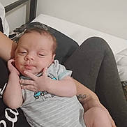 Xavier is registered to the contest to win money with this photo: baby, infant, onesie, sleepy, hand, face, person, adult, arm, clothing, bed, blanket, legs, tattoo, skin, resting, indoors, casual, holding, comfort