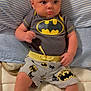 Xavier is registered to the contest to win money with this photo: baby, infant, batman, clothing, shorts, onesie, pillow, striped, cushion, laying, indoors, cute, child, person, portrait, soft, comfortable, casual, relaxed, young