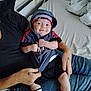 baby, child, hoodie, socks, number_23, smile, person, jeans, bed, blanket, tattoo, indoor, casual, comfort, holding, seated, hand, infant, clothing, relaxed