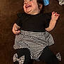 Addisyn is registered to the contest to win money with this photo: baby, infant, child, smiling, laughing, lying_down, black_top, houndstooth_skirt, bow, leggings, brown_blanket, saliva, messy_hair, pile_of_clothes, indoor, cute, portrait, hand, legs, clothing