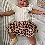 Alani is registered to the contest to win money with this photo: baby, smiling, headband, bow, white_top, leopard_print_skirt, socks, bedspread, striped, lying_down, happy, cute, infant, child, apparel, fashion, indoor, person, portrait, skin
