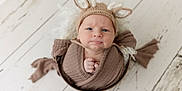 Colton is registered to the contest to win money with this photo: baby, infant, knit_hat, deer_ears, brown_wrap, basket, wooden_floor, cozy, cute, portrait, indoors, child, newborn, wrapped, soft_texture, face, expression, small_hands, headwear, flooring