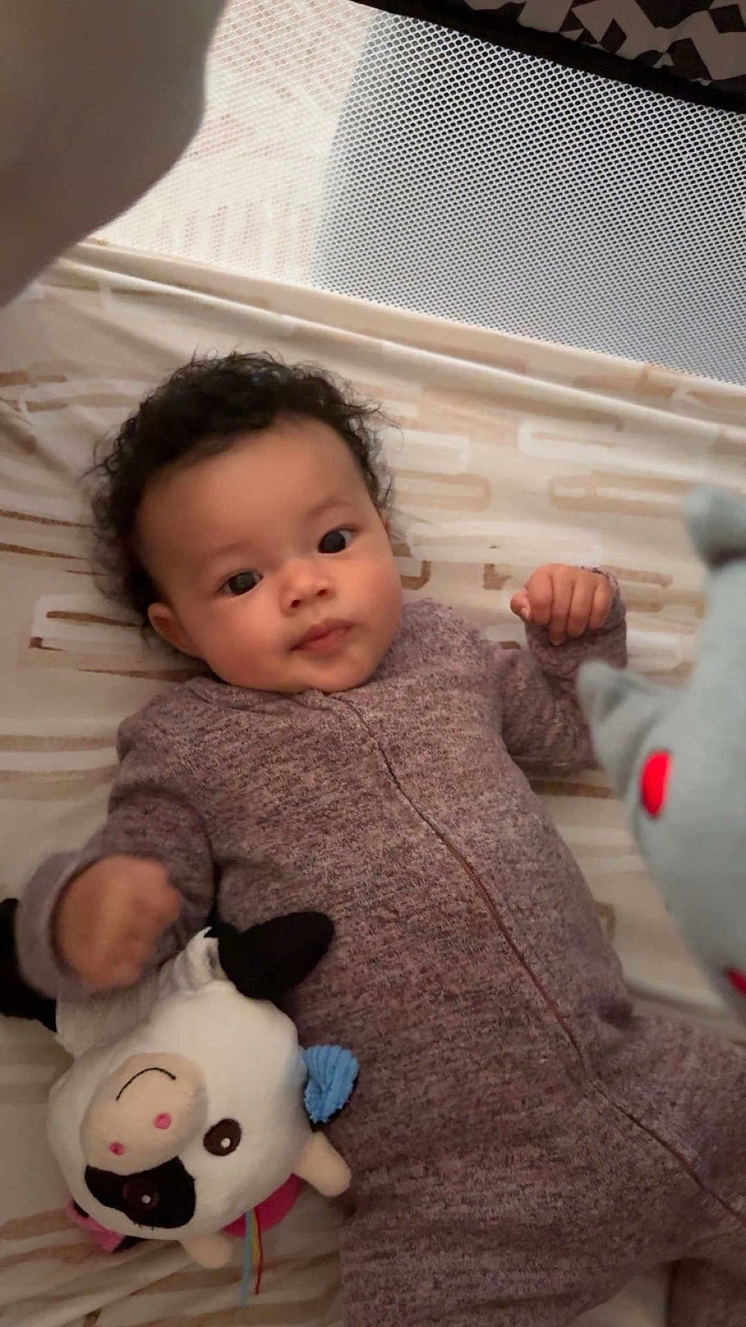 Ryklyn is registered to the contest to win money with this photo: baby, infant, onesie, plush_toy, cow_toy, bed, sheet, pattern, face, hand, curly_hair, lying_down, indoor, soft_toy, child, cute, cozy, sleepwear, playtime, young