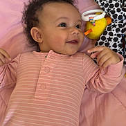 Ryklyn joined the competition — help win amazing prizes! baby, infant, pink_onesie, blanket, smiling, toy, plush_toy, curly_hair, lying_down, child, soft_texture, indoor, cute, happy, patterned_toy, black_and_white, yellow_toy, playful, portrait, closeup