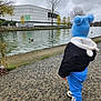 Mathias-Gabriel a rejoint le concours — aidez-le/la à gagner de superbes lots ! toddler, child, blue_clothing, blue_hat, pom_poms, canal, water, duck, cloudy_sky, autumn_trees, urban, building, pathway, outdoor, nature, footwear, winter_clothing, person, standing, scenery