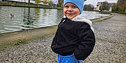 Mathias-Gabriel participe au concours pour gagner de l'argent avec cette photo : toddler, child, blue_hat, black_jacket, blue_pants, sneakers, outdoor, canal, pathway, overcast, trees, water, urban, smiling, cute, winter_clothing, standing, person, playful, park