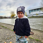 Mathias-Gabriel participe au concours pour gagner de l'argent avec cette photo : toddler, child, outdoor, river, cloudy_sky, hat, jacket, pants, sneakers, sidewalk, building, nature, autumn, leaves, casual_clothing, portrait, walking, young_child, urban, daytime
