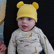 Mayshkan participe au concours pour gagner de l'argent avec cette photo : baby, child, yellow_hat, bear_ears, animal_print, shirt, pants, blue_eyes, smiling, face, hand, chair, cushion, indoor, curious, seated, cute, playful, infant, clothing