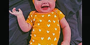 Renesmae joined the competition — help win amazing prizes! apparel, baby, bed, blanket, bow, cheerful, child, cute, fabric, face, hand, happy, headband, infant, lying_down, orange_onesie, person, skin, smiling, toddler