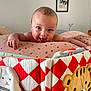 baby, infant, smiling, tongue_out, cushion, patterned_fabric, quilt, tiger_design, bunny_design, wall_art, dog_painting, indoor, person, face, head, happy, cute, child, room, furniture