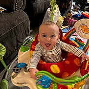 Declan is registered to the contest to win money with this photo: activity_jumper, baby, child, clothing, colorful, couch, development, floor, furniture, happy, home, indoor, infant, joy, living_room, person, play, smiling, striped_shirt, toy