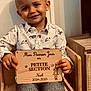 child, boy, smiling, shirt, wooden_sign, chair, indoor, portrait, face, hands, clothing, wood, furniture, happy, cute, person, casual, home, background, young