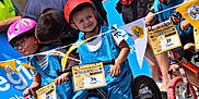 Naël participe au concours pour gagner de l'argent avec cette photo : child, children, helmet, bicycle, balance_bike, race, outdoor, smiling, blue_jersey, number_tag, flag, sport, competition, event, person, happy, team, glasses, helmet_strap, casual_clothing