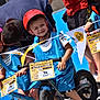 child, children, helmet, bicycle, balance_bike, race, outdoor, smiling, blue_jersey, number_tag, flag, sport, competition, event, person, happy, team, glasses, helmet_strap, casual_clothing