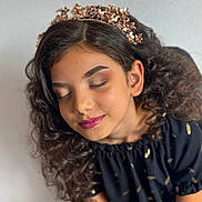 Annais a rejoint le concours — aidez-le/la à gagner de superbes lots ! child, girl, curly_hair, crown, flower_crown, closed_eyes, makeup, lipstick, black_dress, golden_pattern, portrait, peaceful, soft_light, smiling, young, fashion, indoors, beauty, long_hair, cute