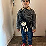 child, boy, indoor, door, hat, beanie, batman_logo, jacket, denim, teddy_bear, bag, jeans, red_shoes, sneakers, floor, wall, casual_clothing, standing, portrait, young