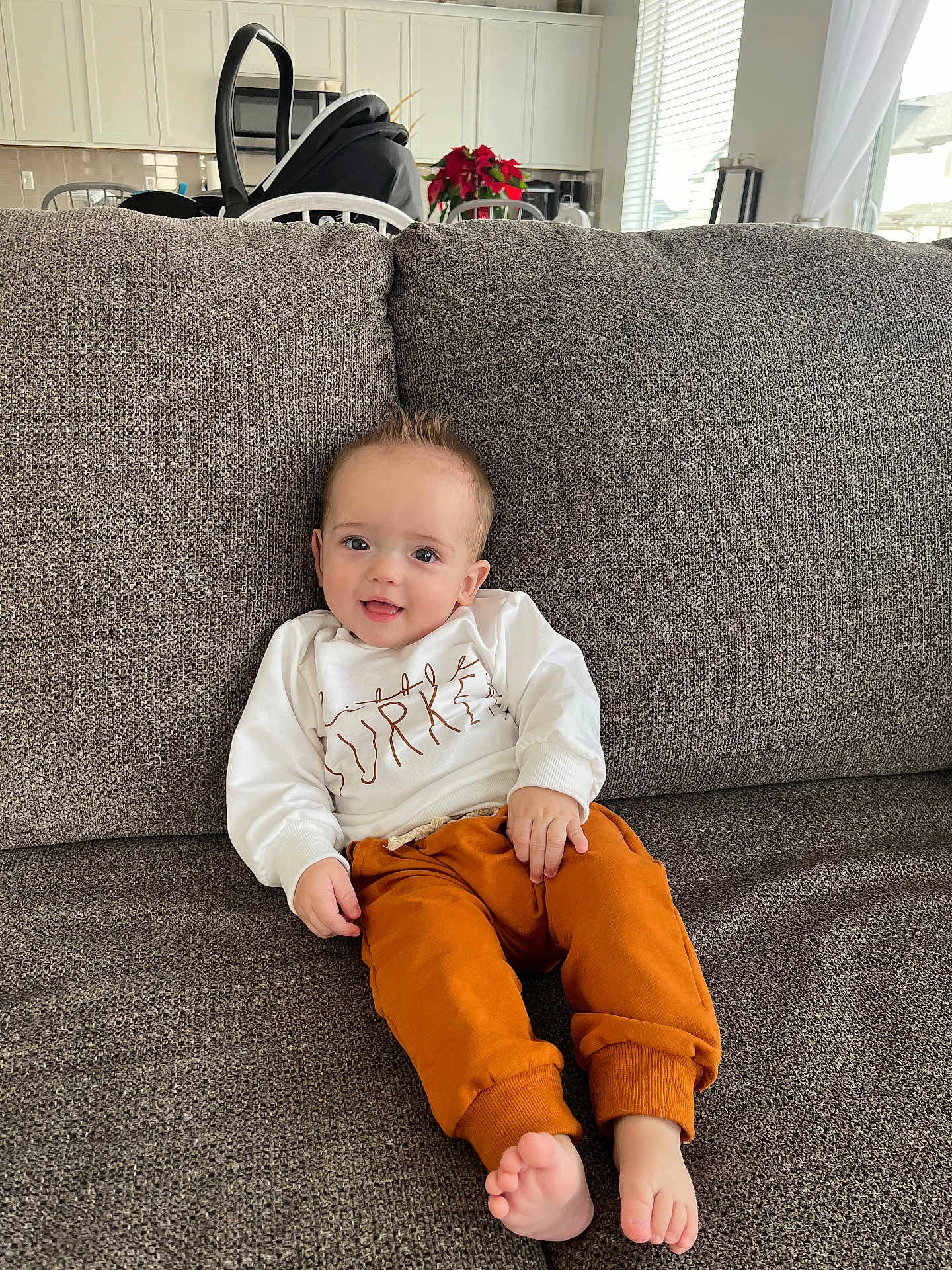 Bo G joined the competition — help win amazing prizes! baby, child, couch, sweatshirt, pants, barefoot, smile, indoor, home, furniture, infant, relaxing, happy, casual_clothing, person, cute, small_person, seated, living_room, cozy